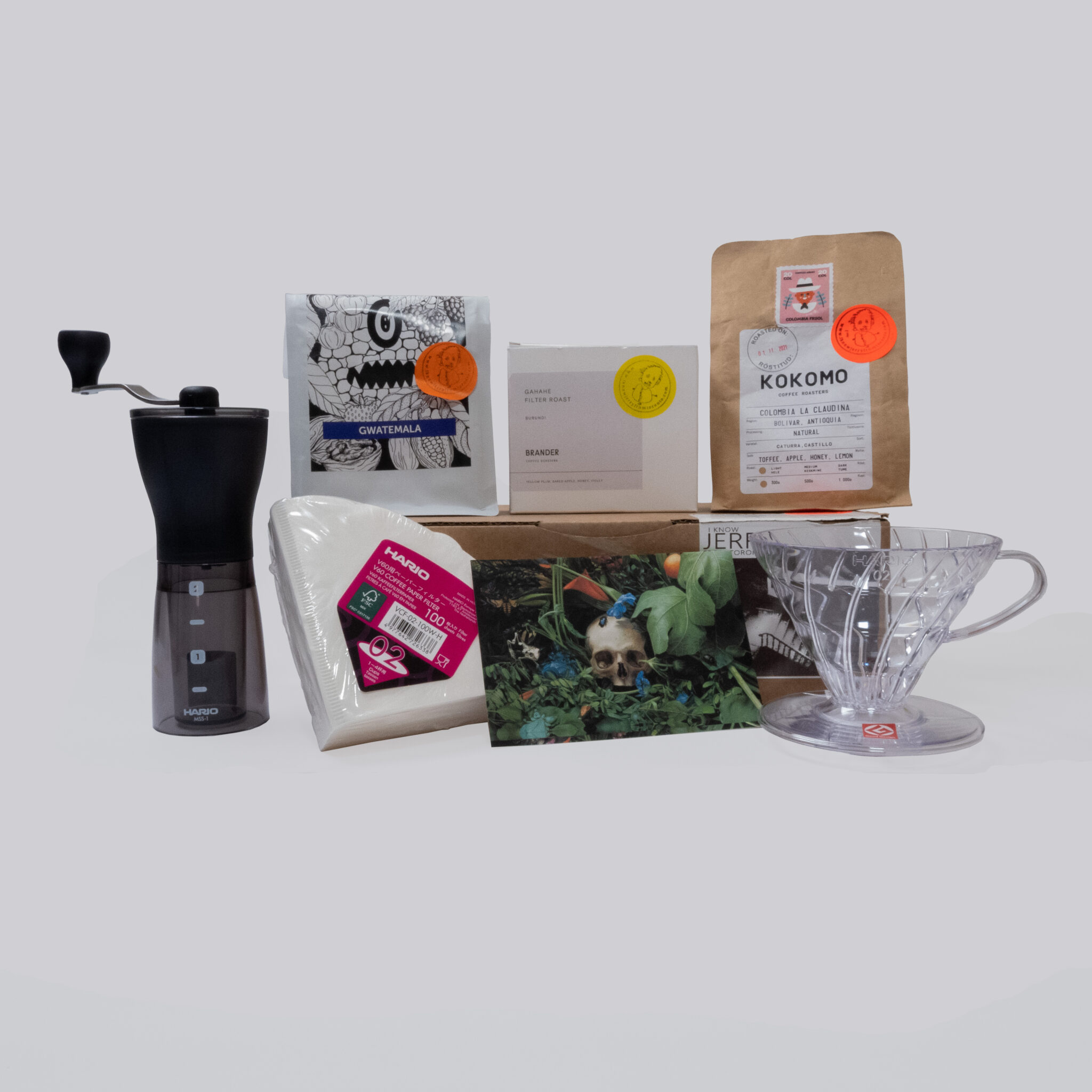 Packshot of the Full Summit Coffee box with coffee from Kokomo, Brander, Coffee Proficiency and an artwork of Cindy Wright, a Hario grinder, Plastic V60 dripper and a pack of V60-02 paper filters
